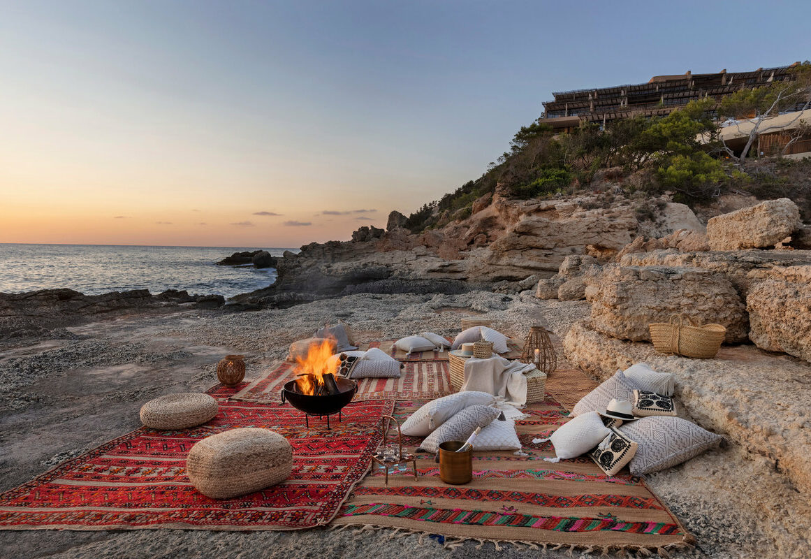 a group of pillows on a rug on a beach with a fire